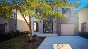 A modern two-story house with a garage, a tree in the front yard, and a clear sky. - Private Yoga Space & Cold Plunge Near Everglades (Florida City)