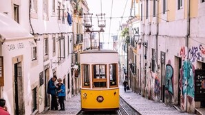 A yellow tram on tracks in a narrow street with buildings on either side. - Surfbase Lisbon (Almada)