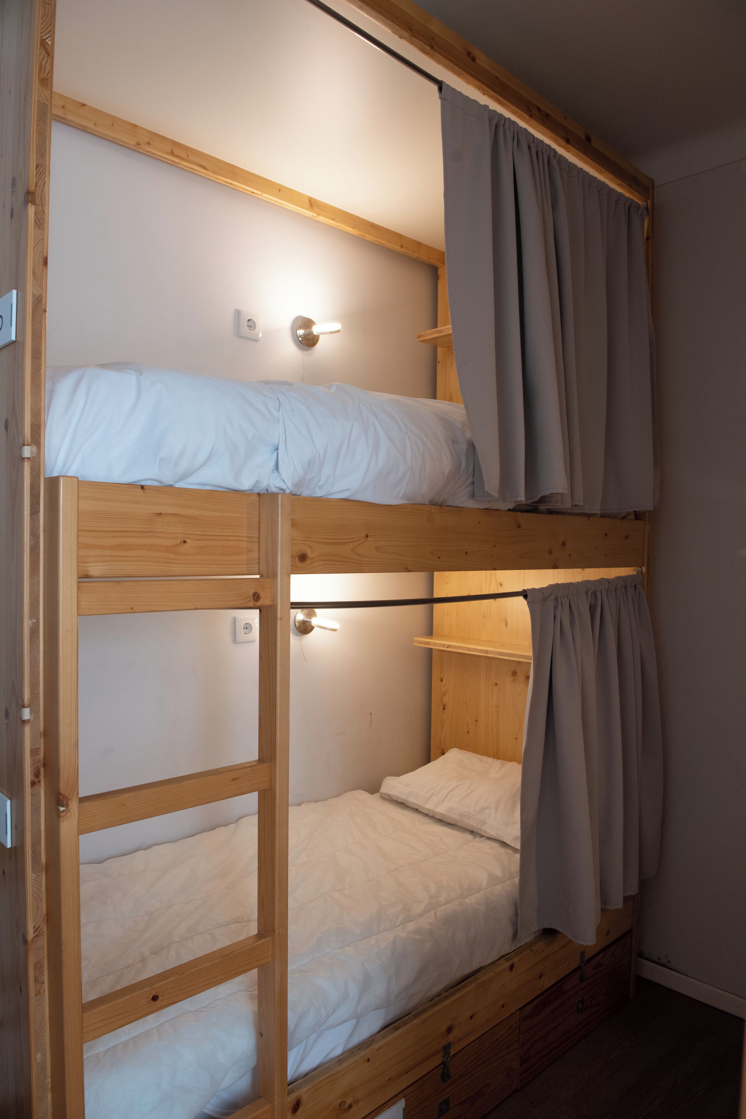 A bunk bed with a wooden frame, a lower bunk, and a top bunk. There is a light fixture on the wall above the top bunk.