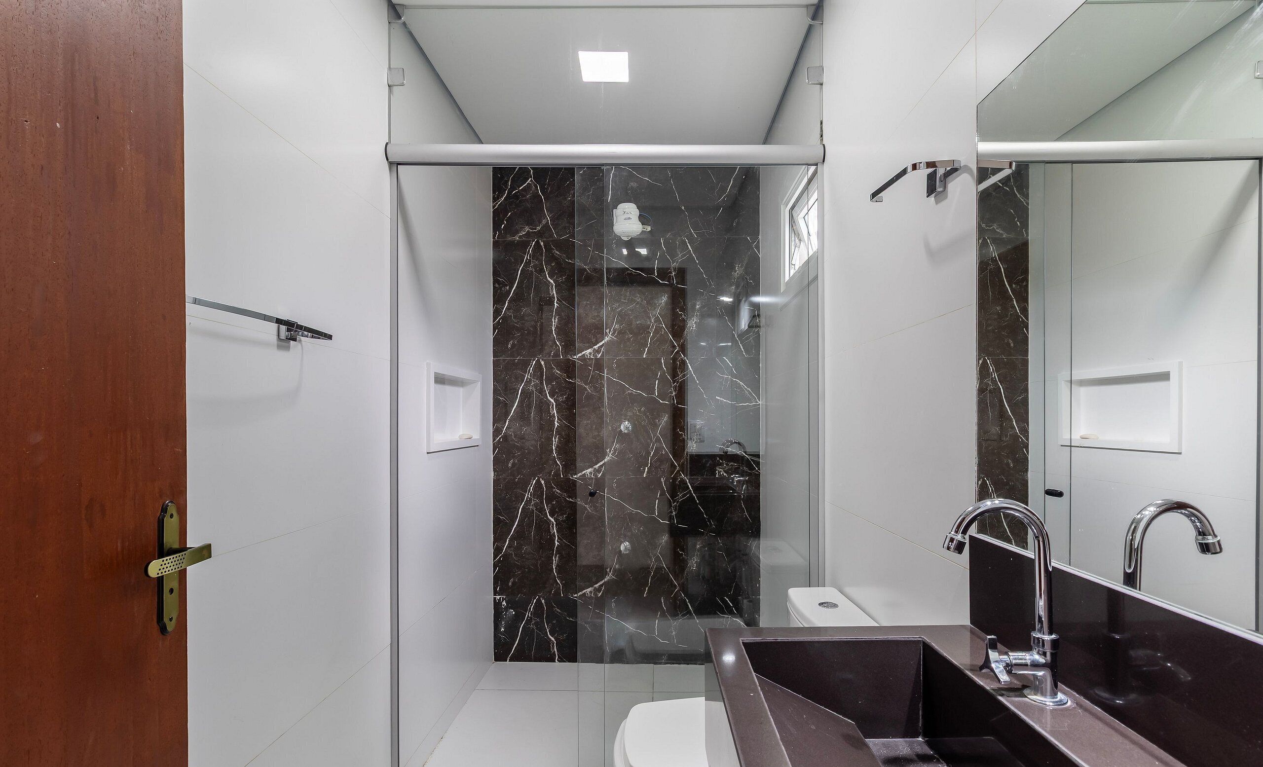 A modern bathroom with a glass shower enclosure, a white toilet, a dark sink with a mirror, and a marble backsplash.