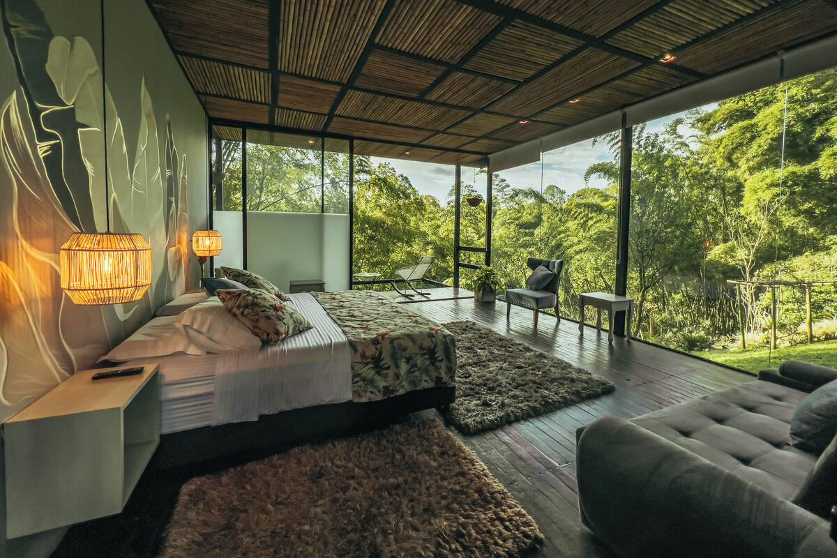 Une chambre moderne avec un grand lit, un canapé et une vue sur un paysage verdoyant.