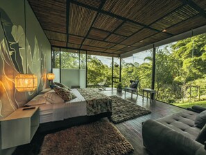 Un dormitorio moderno con una cama grande, un sofá y vistas a exuberante follaje exterior.