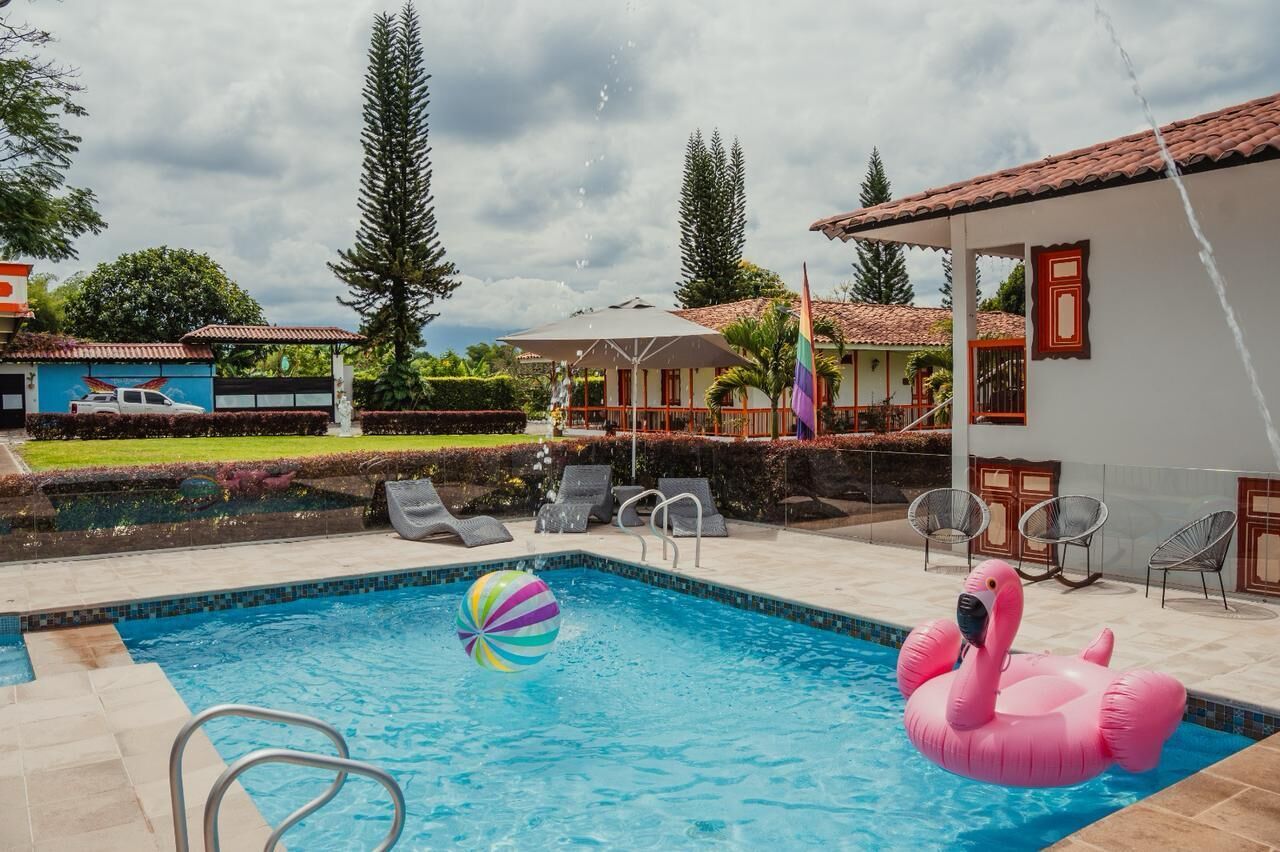 Una piscina con un flotador en forma de flamenco rosa y una pelota de playa, rodeada de sillas de descanso y una zona techada.