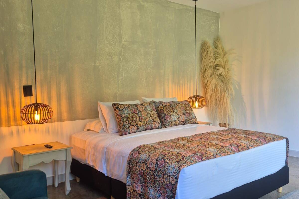 Une chambre moderne avec un grand lit, des tables de chevet, une petite table d’appoint, un canapé et une grande plante décorative.