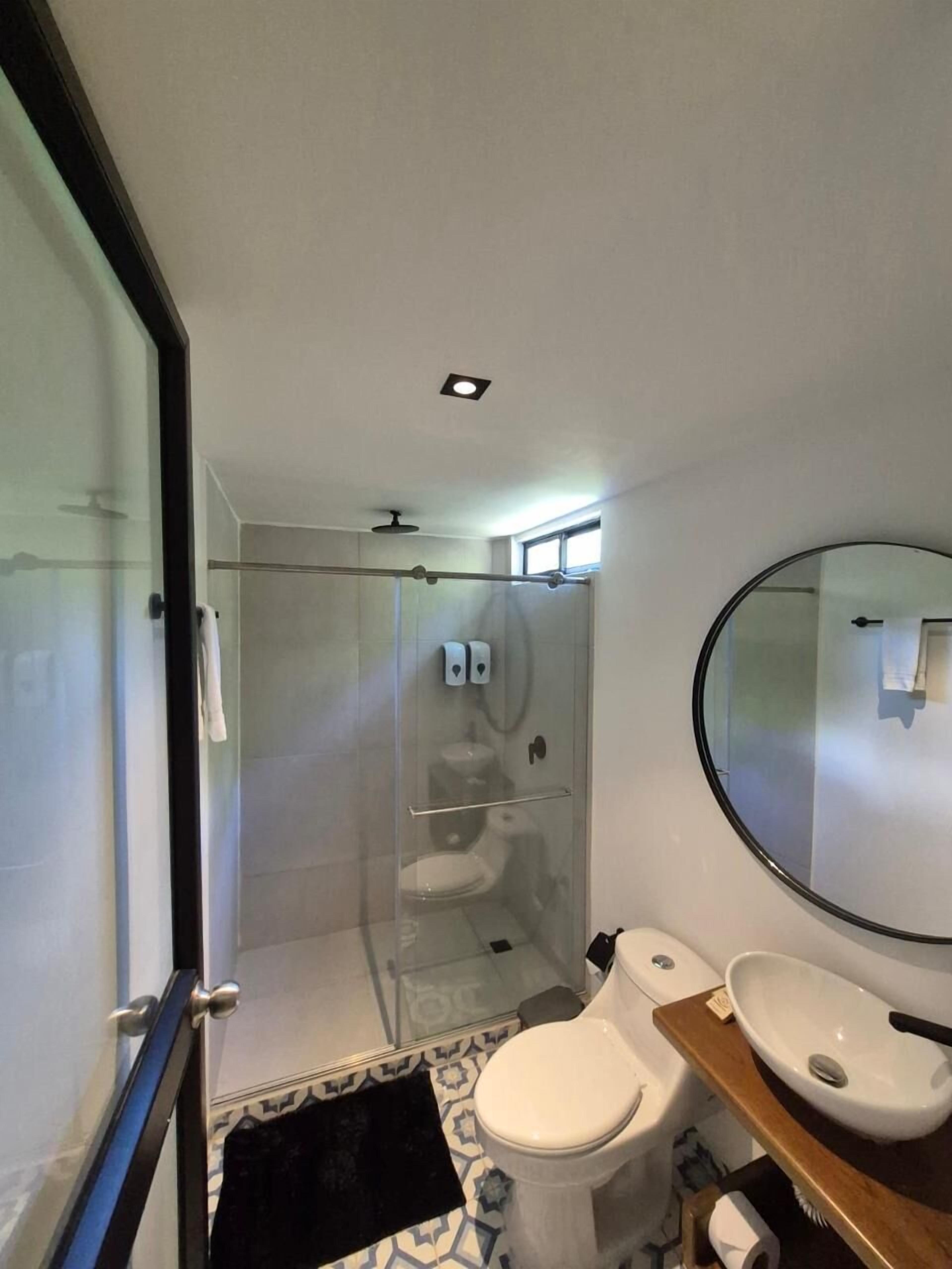 A modern bathroom with a glass-enclosed shower, a white toilet, and a round mirror.