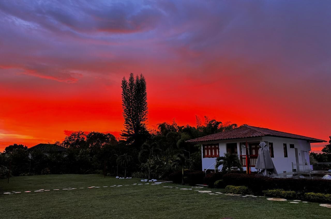 A house with a red roof, surrounded by a well-maintained lawn and trees, under a sunset sky.