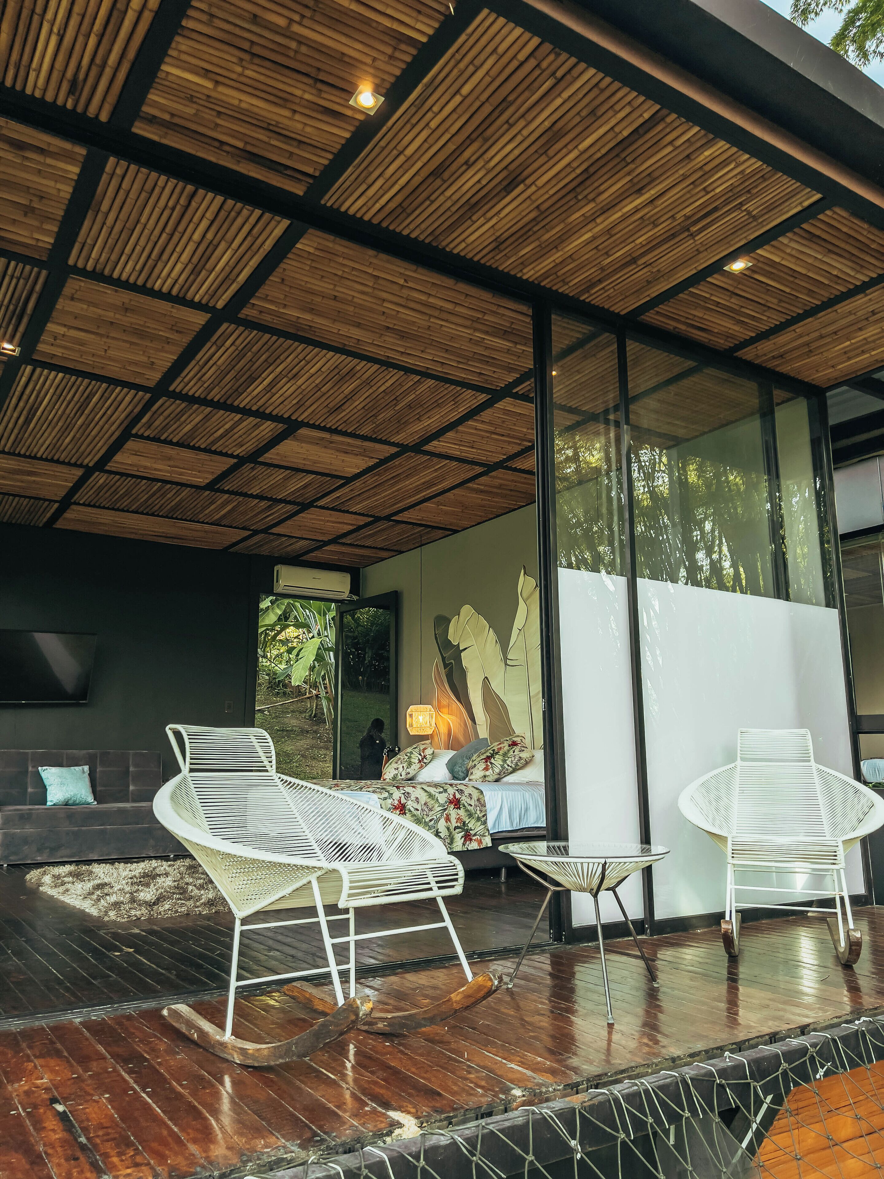 Un espacio exterior moderno con techo de madera, un sofá y dos sillones.