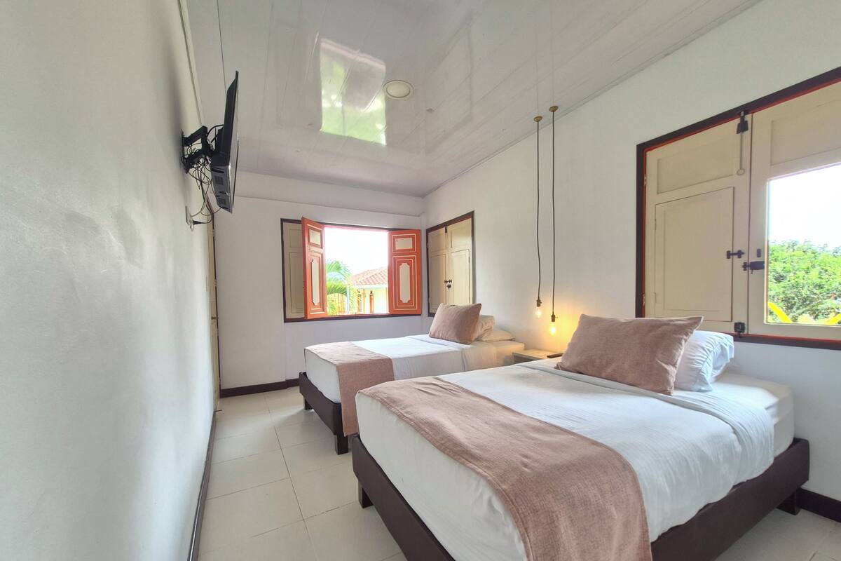 Une chambre avec deux lits, un téléviseur fixé au mur et une fenêtre donnant sur un paysage verdoyant.