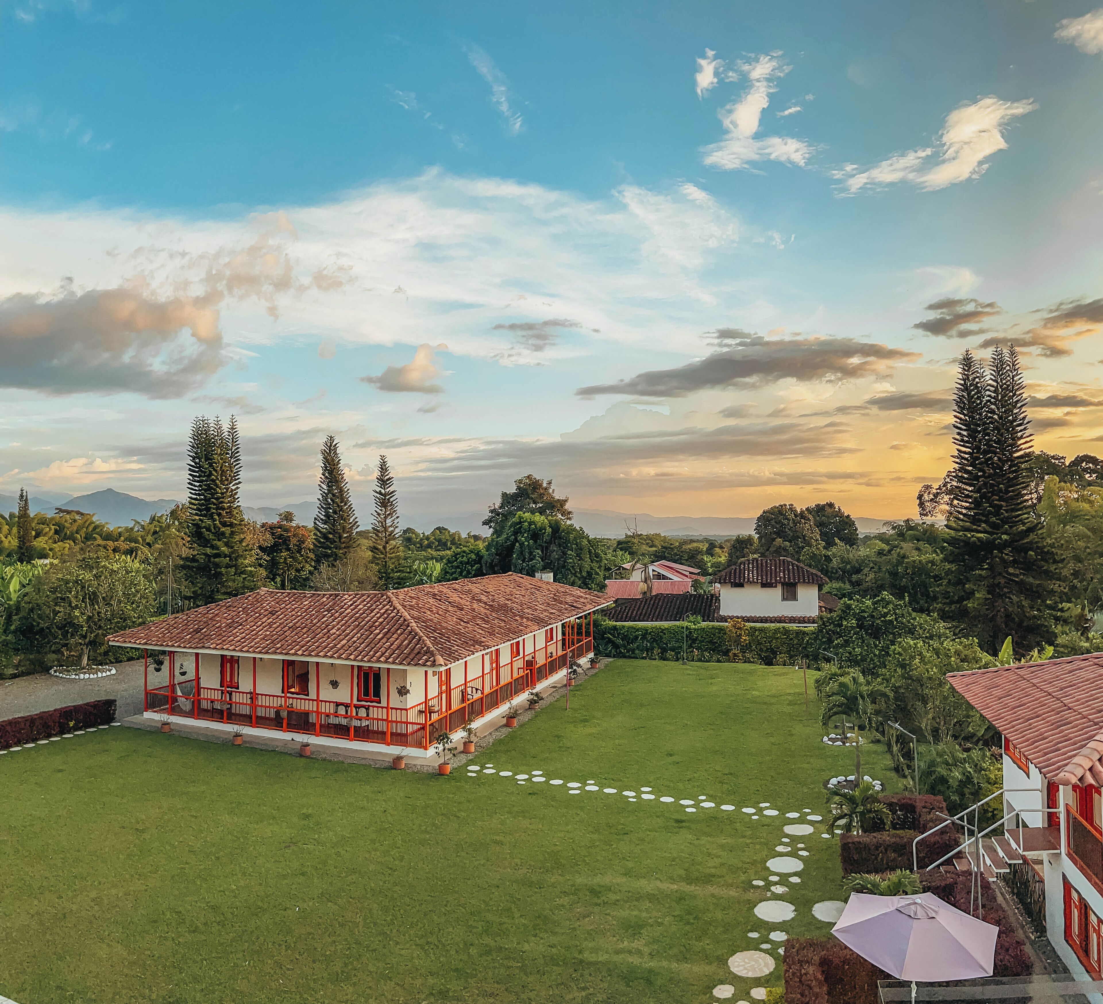 A large, open house with a red-tiled roof, surrounded by a well-maintained lawn and several trees.