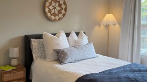 Et pænt møbleret soveværelse med seng, sengeborde, en lampe og et dekorativt vægkunstværk.