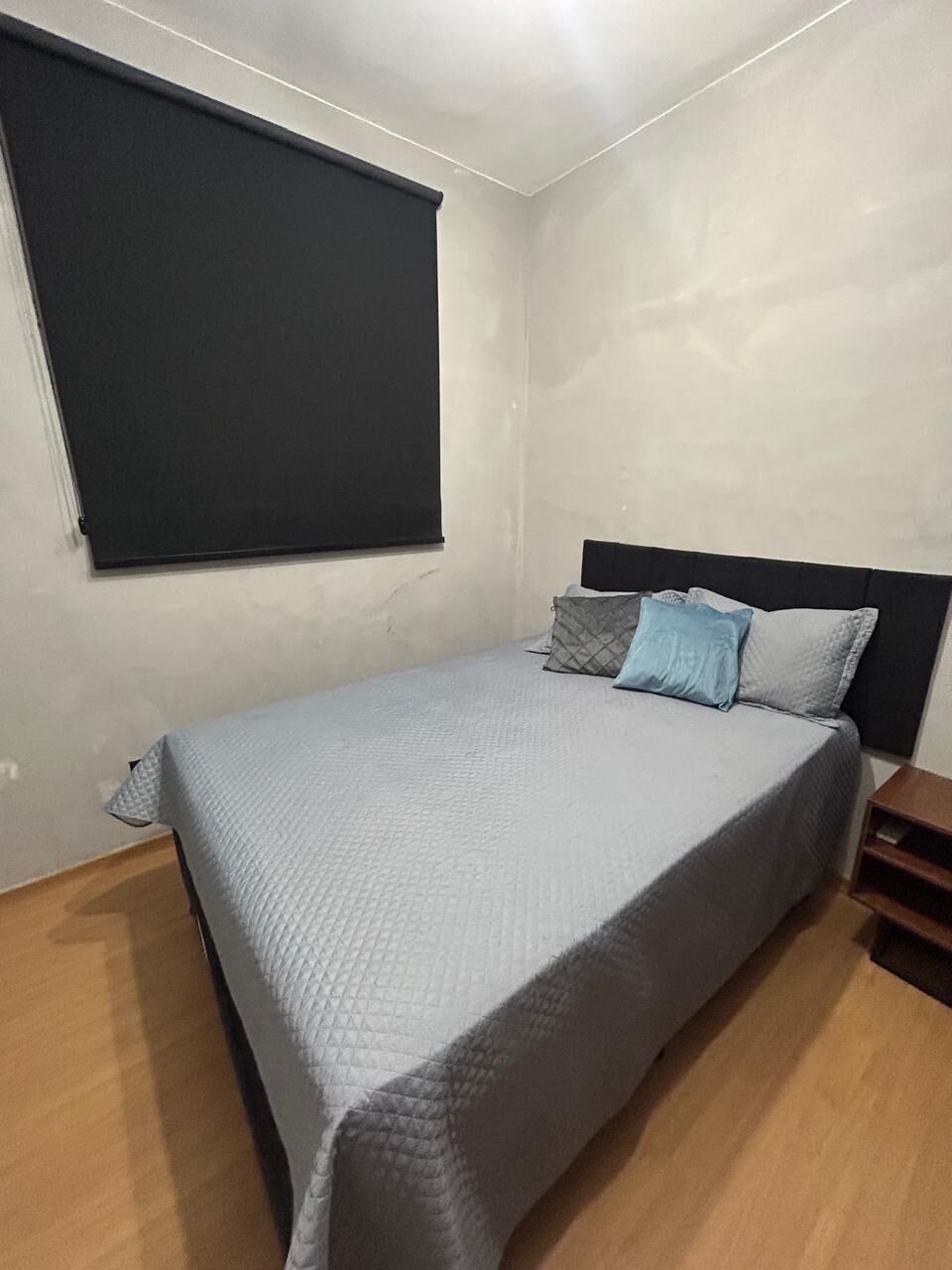 A bedroom with a bed, a headboard, a window with a blind, and a wooden floor.
