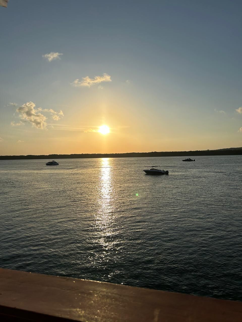 A calm body of water with boats and a clear sky during sunset.