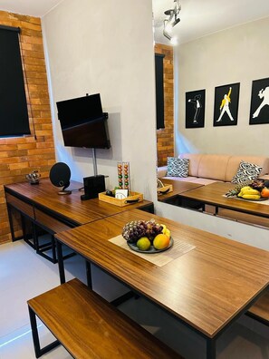 A modern living room with a long wooden table, a flat-screen TV, a brick wall, and a sofa with patterned cushions. - 1003 Apto 2 Qtos João Pessoa Cabedelo (Cabedelo)