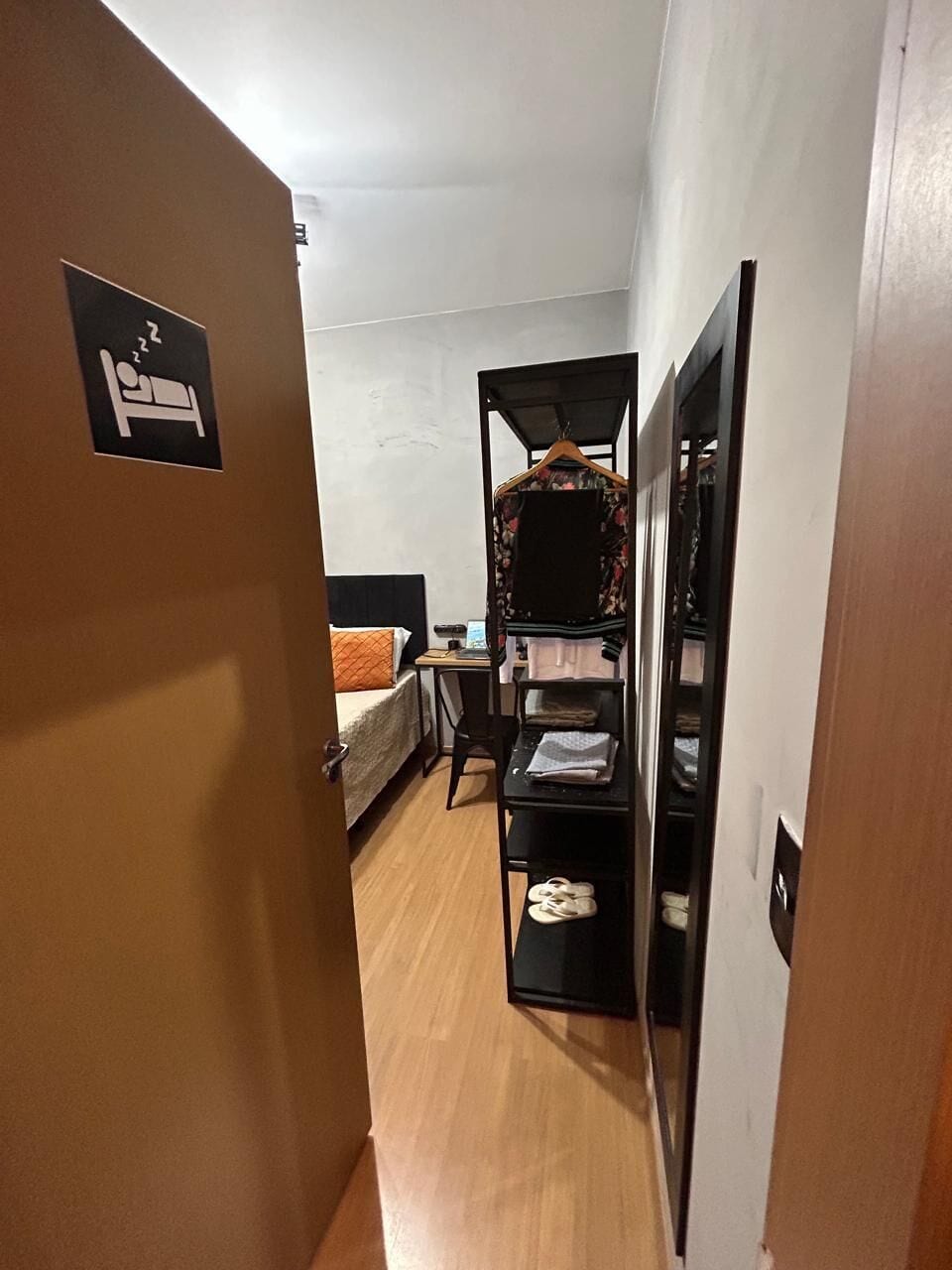 A narrow hallway with a bed, a desk, and a hanging wardrobe.