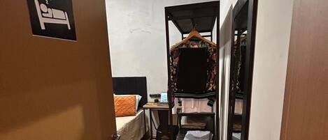 A narrow hallway with a bed, a desk, and a hanging wardrobe.