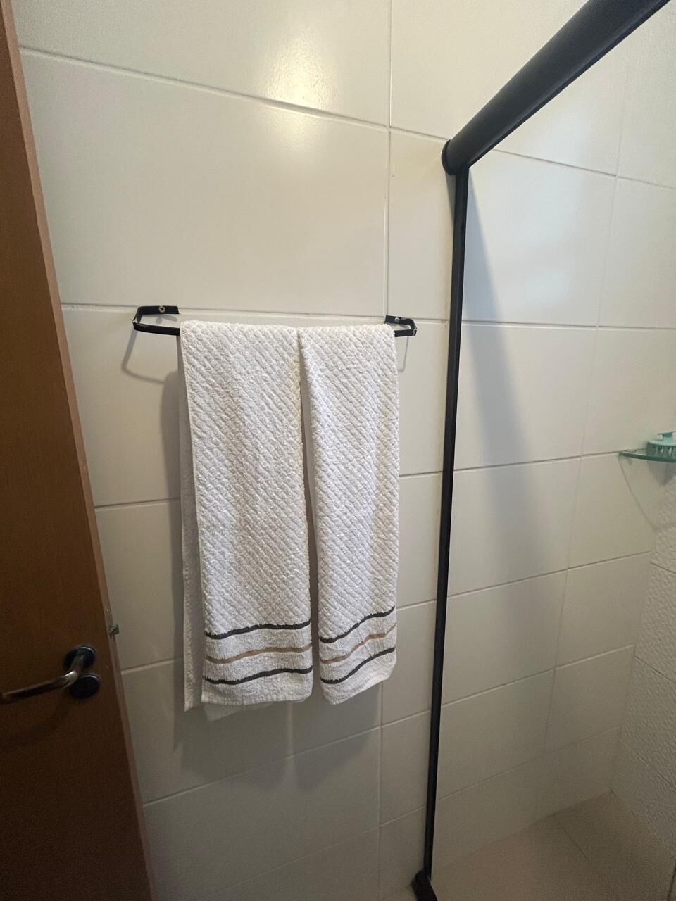 A bathroom with white tiled walls, a black towel rack with two towels, and a shower area.