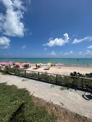 A beach with umbrellas and people, a clear sky, and a calm sea.