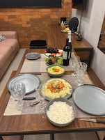 Mesa de comedor lista con platos, tazones y una botella de vino, indicando un ambiente para comer.