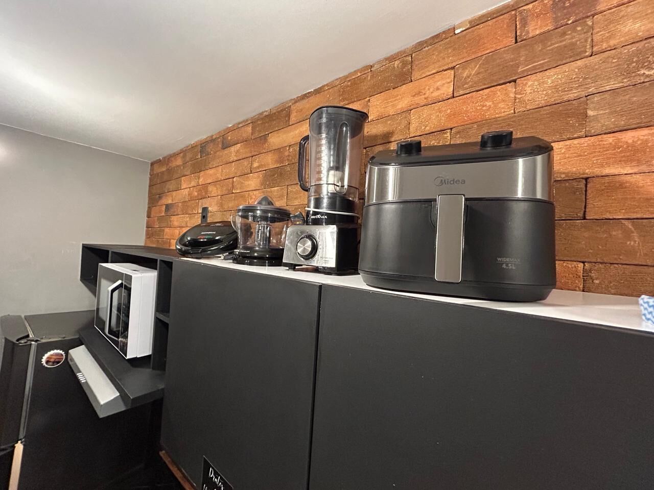 Une cuisine avec un mur en briques, une machine à café, un mixeur et un four à micro-ondes.