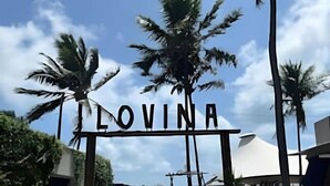 Ein Schild mit der Aufschrift 'LOVINA' am Eingang eines Resorts mit Palmen und blauem Himmel.