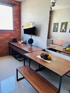 A modern living room with a flat-screen TV, a wooden dining table, benches, a sofa, and a coffee table with fruit. - 1003 Apto 2 Qtos João Pessoa Cabedelo (Cabedelo)