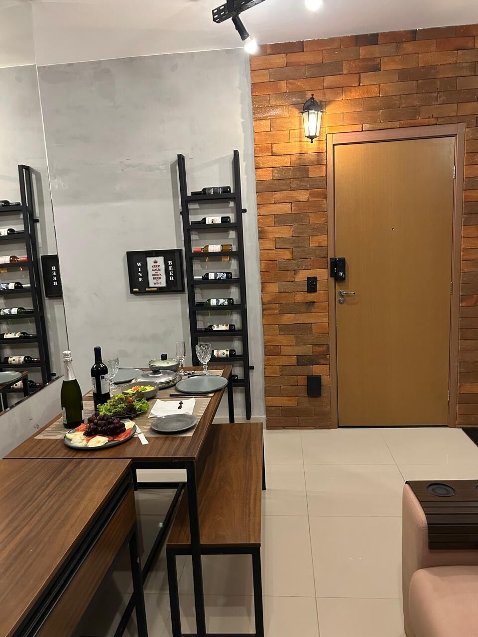 A modern kitchen with a wooden table set for dining, a wine rack, and a door with a light fixture.
