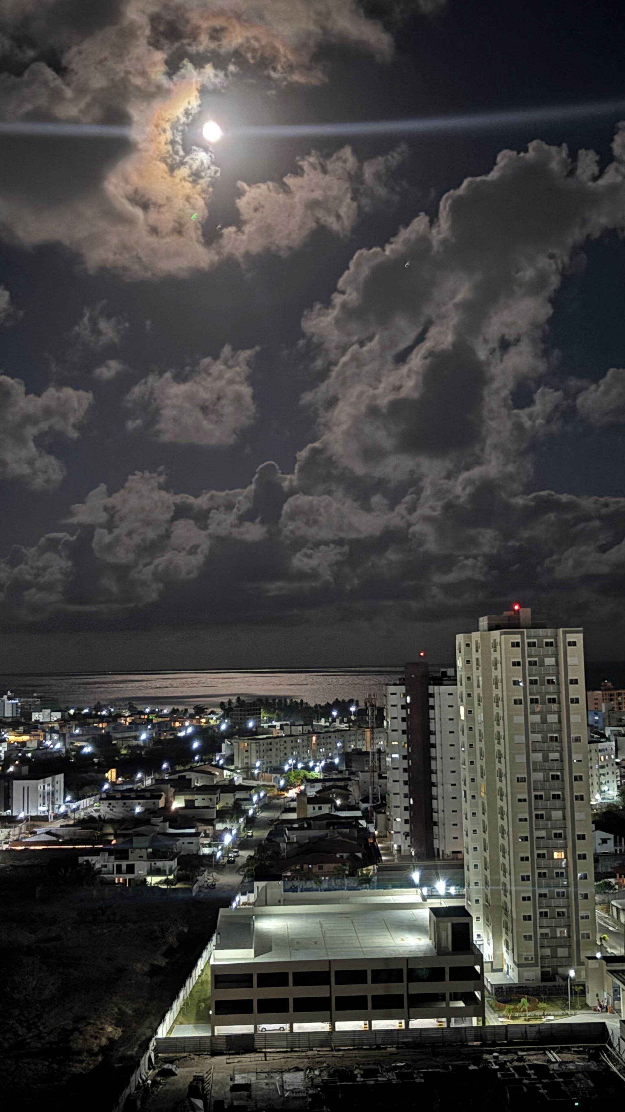 A nighttime cityscape with a full moon, clouds, and illuminated buildings.