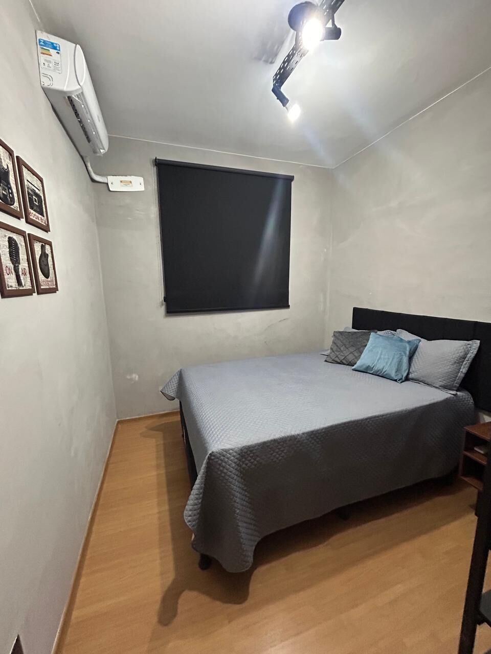 A bedroom with a bed, a ceiling light, an air conditioner, and a window with a blind.