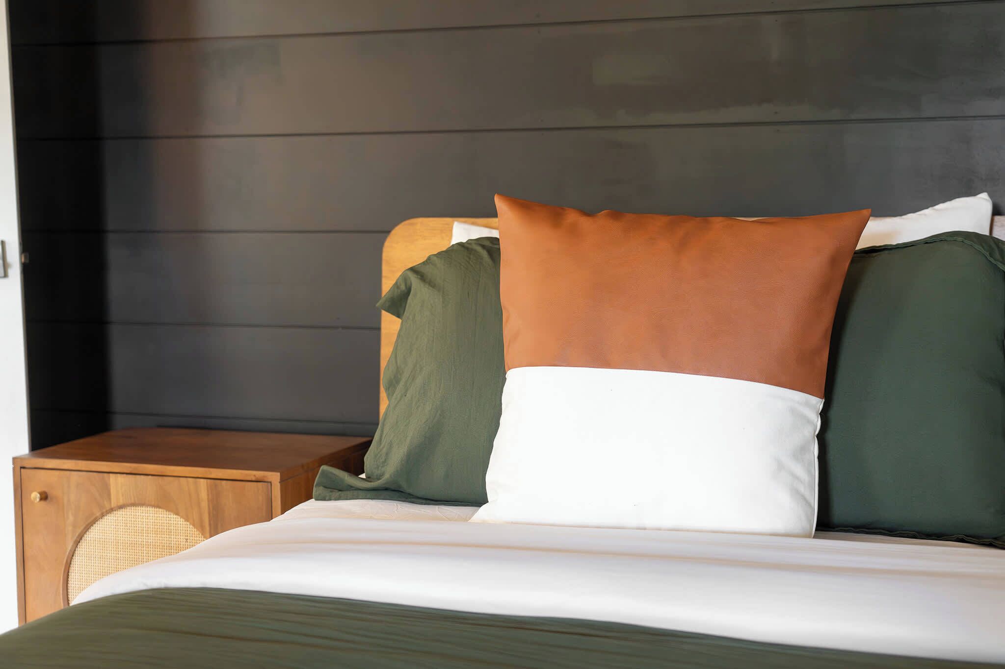 Una cama con colcha blanca y verde, una mesita de noche de madera y una silla de mimbre, junto a un cabecero de madera oscura.