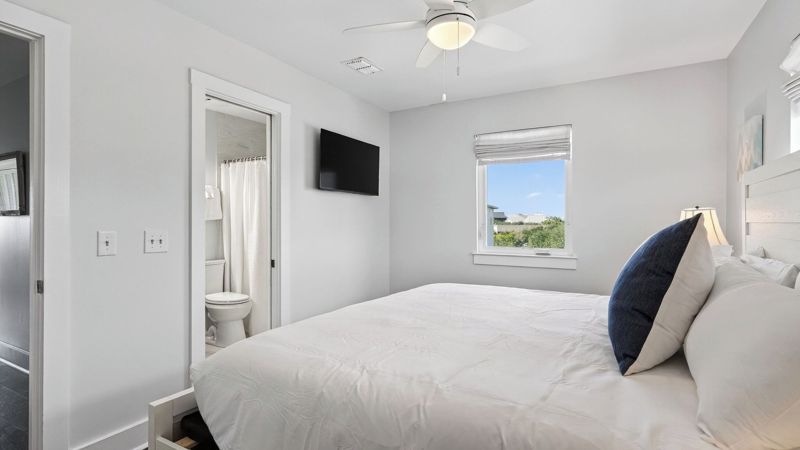 Ein Schlafzimmer mit Bett, Fernseher, Fenster und Deckenventilator.