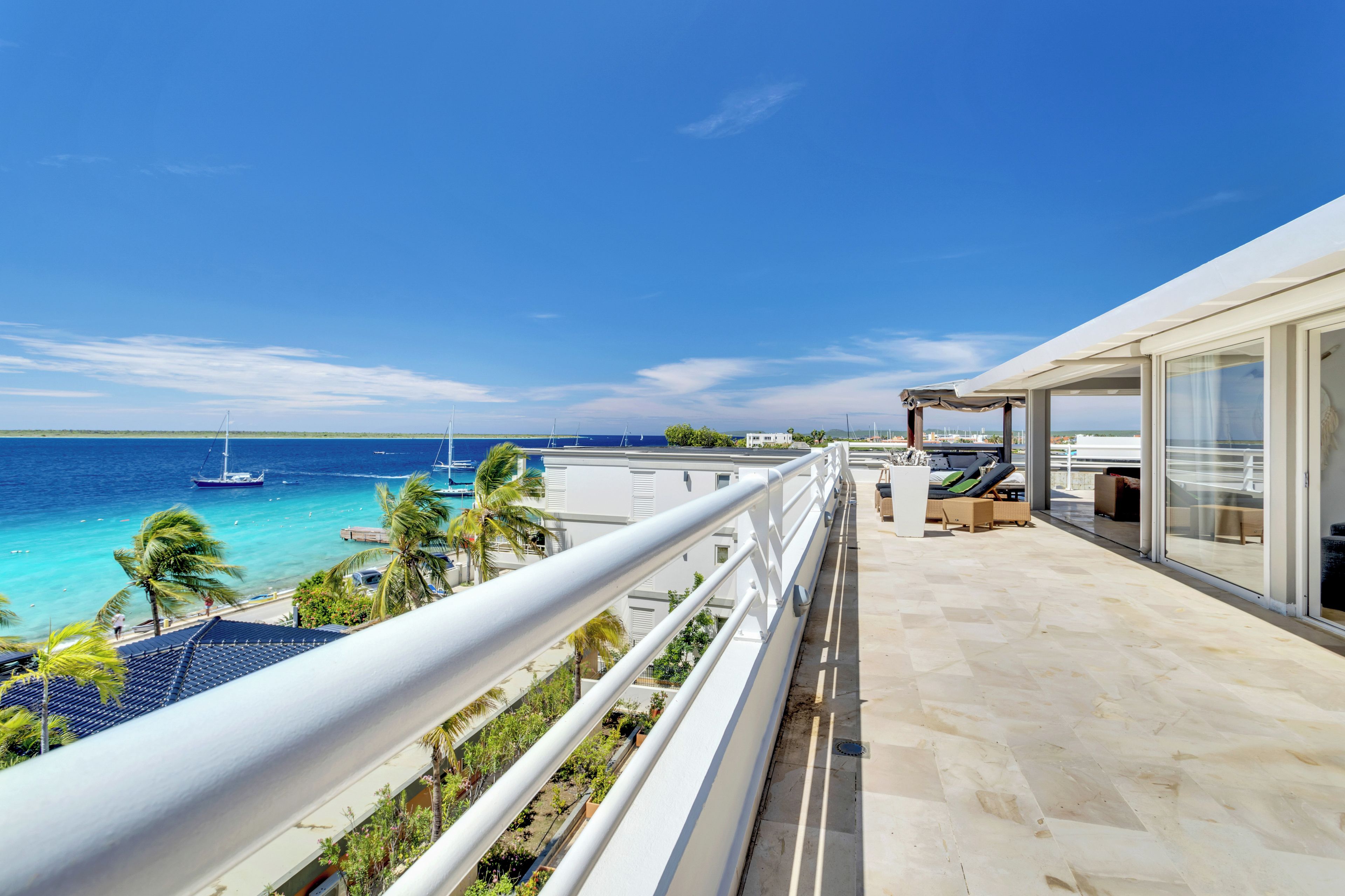 A balcony with a view of the sea and boats, a covered seating area, and a glass door leading to a room.