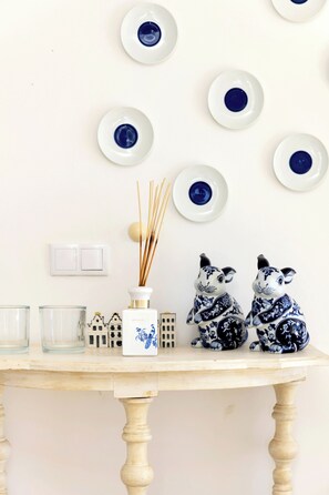 A table with decorative items, including ceramic rabbits and a vase with reeds, set against a wall with several white plates with blue centers. - Sea Side Penthouse (kralendijk)