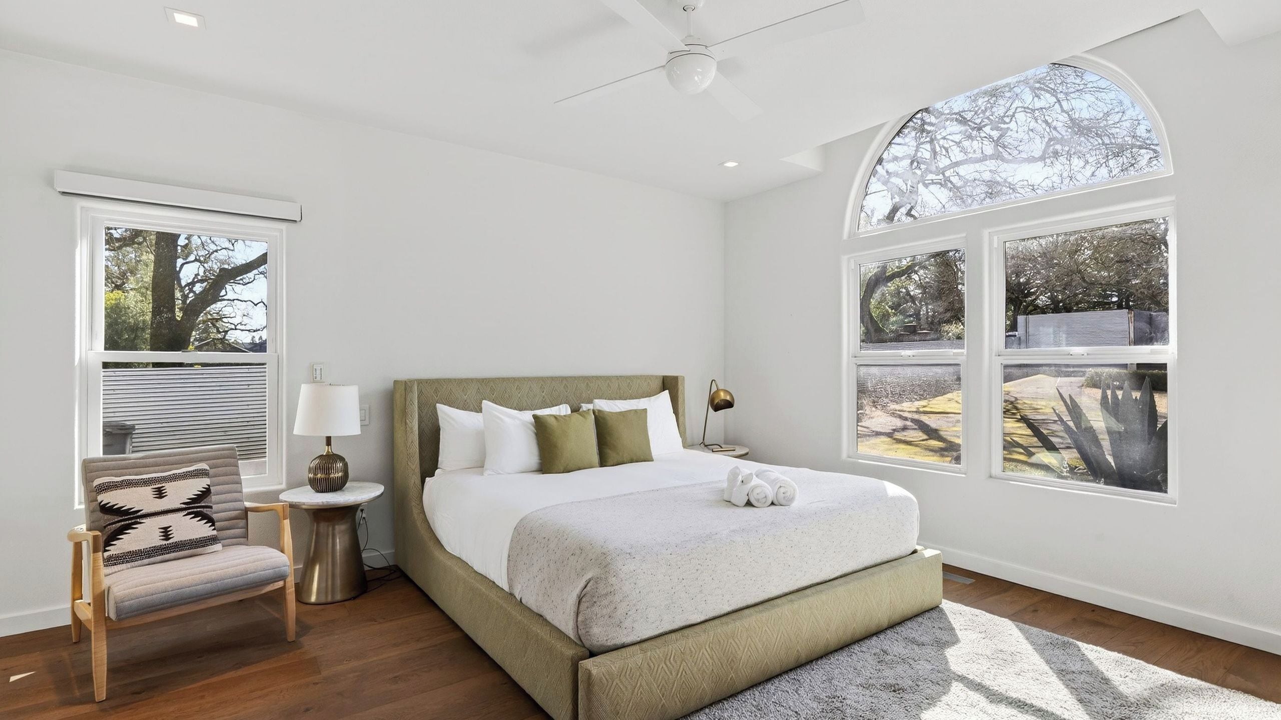 Un dormitorio con cama, una silla, una lámpara y ventanas amplias.