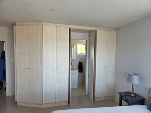 Un dormitorio con cama, mesita de noche con lámpara, armario y baño visible a través de una puerta abierta.