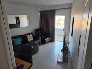 A living room with a sofa, a television, and a sliding glass door leading to a balcony.