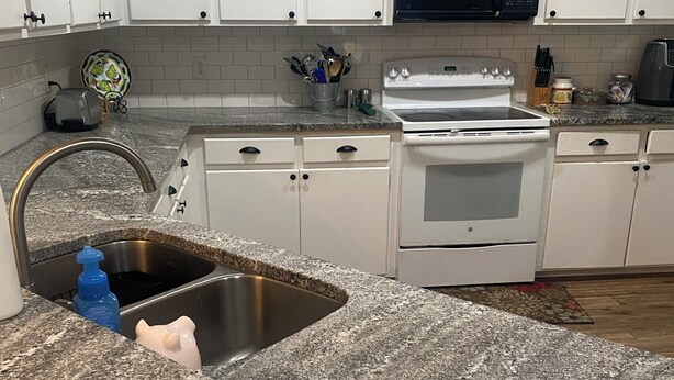 A kitchen with white cabinets, a granite countertop, a stainless steel sink, a microwave, and a stove. - Peaceful and Cozy 3 Bedroom house on the water in Bay St Louis! Sleeps 6. (Bay St. Louis)
