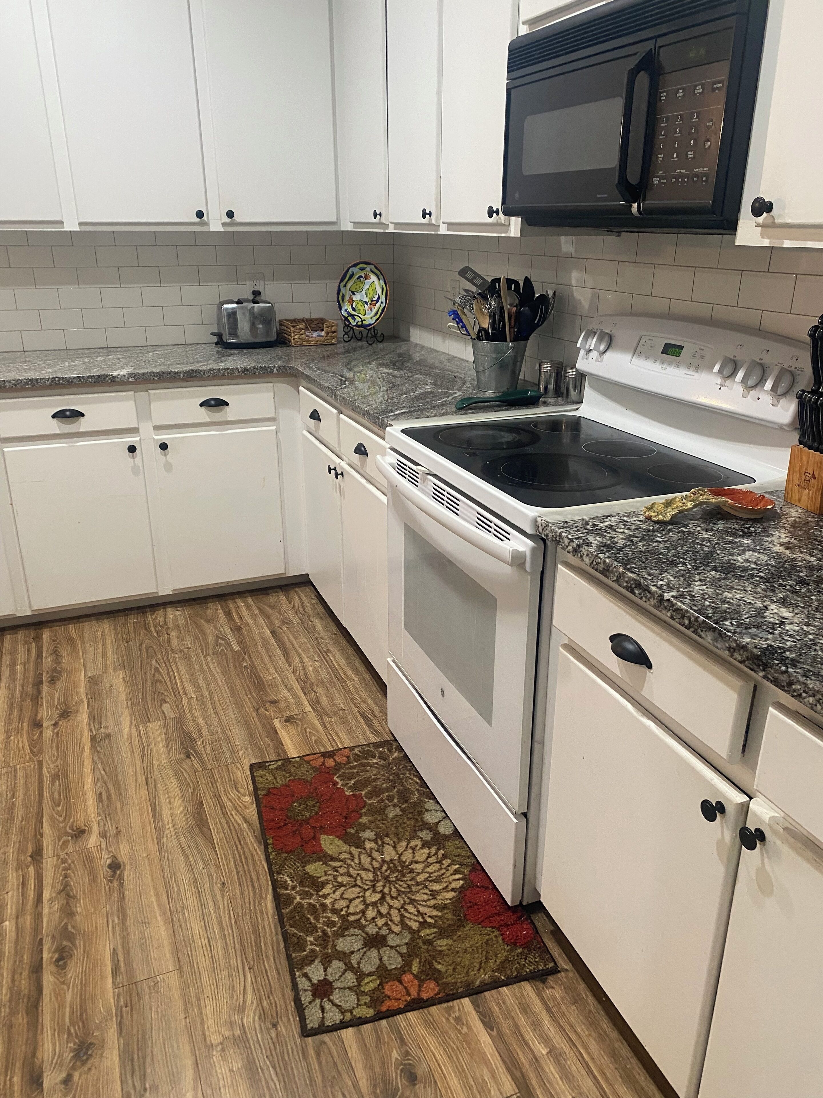A kitchen with white cabinets, a granite countertop, a microwave, a stove, and a wooden floor.