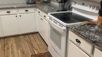 A kitchen with white cabinets, a granite countertop, a microwave, a stove, and a wooden floor.