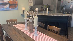 A dining area with a wooden table, chairs, a red and white striped table runner, and a vase with cotton plants. - Peaceful and Cozy 3 Bedroom house on the water in Bay St Louis! Sleeps 6. (Bay St. Louis)