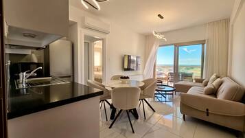 A modern living room with a sofa, dining area, kitchen, and a balcony with a view.