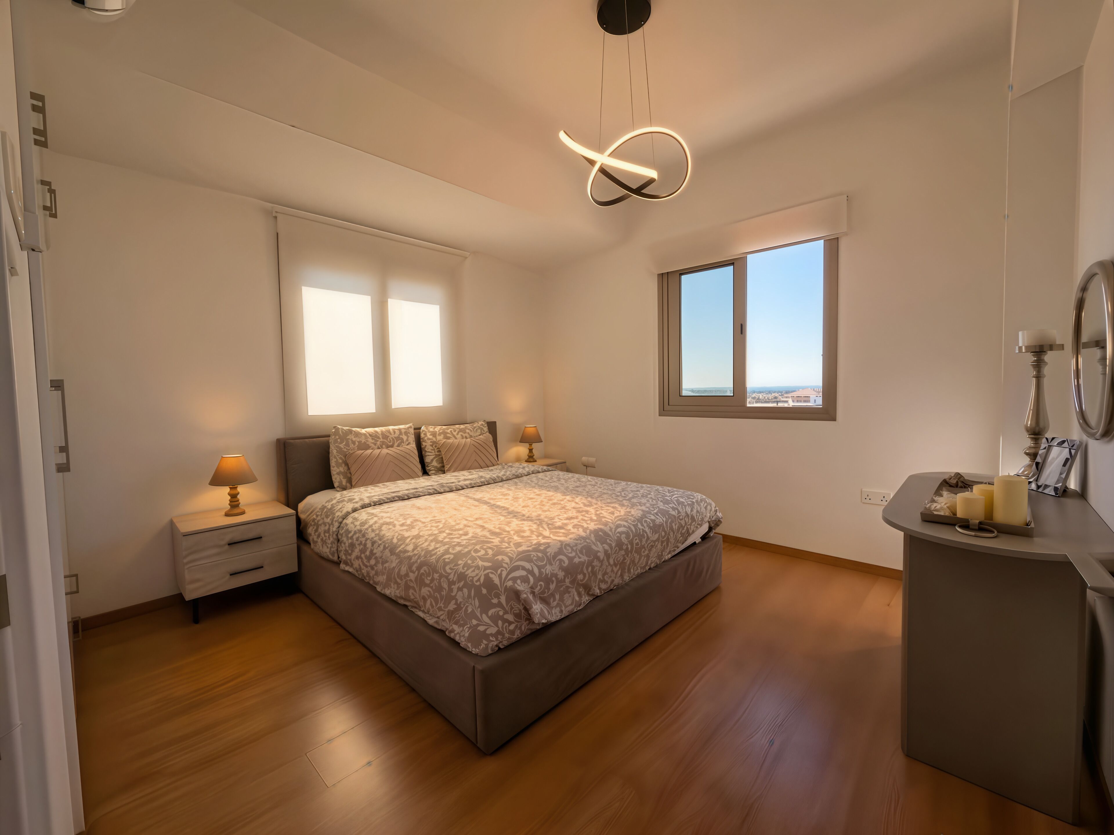 A bedroom with a bed, bedside tables, a nightstand, a mirror, and a window with a view.