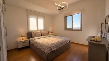 A bedroom with a bed, bedside tables, a nightstand, a mirror, and a window with a view.