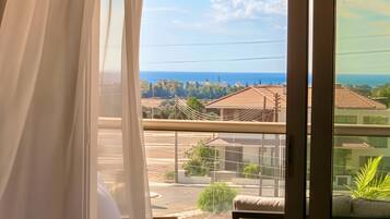 A balcony with a view of the sea, a chair, a table, and a curtain.