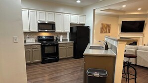 A modern kitchen with white cabinets, a black refrigerator, a microwave, and an oven. There's a trash can and a bar stool in the corner. - 5 min Walk to GWCC, Mercedes-Benz, World Cup! (Atlanta)
