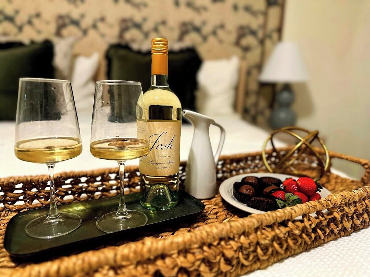 A tray with two glasses of white wine, a bottle of wine, a pitcher, and a plate of strawberries and chocolate.