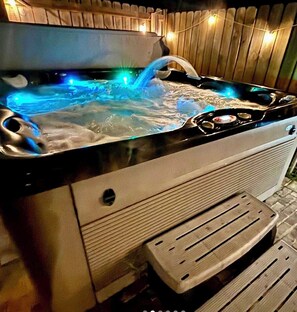 Un jacuzzi con muelle de madera y luces cálidas.