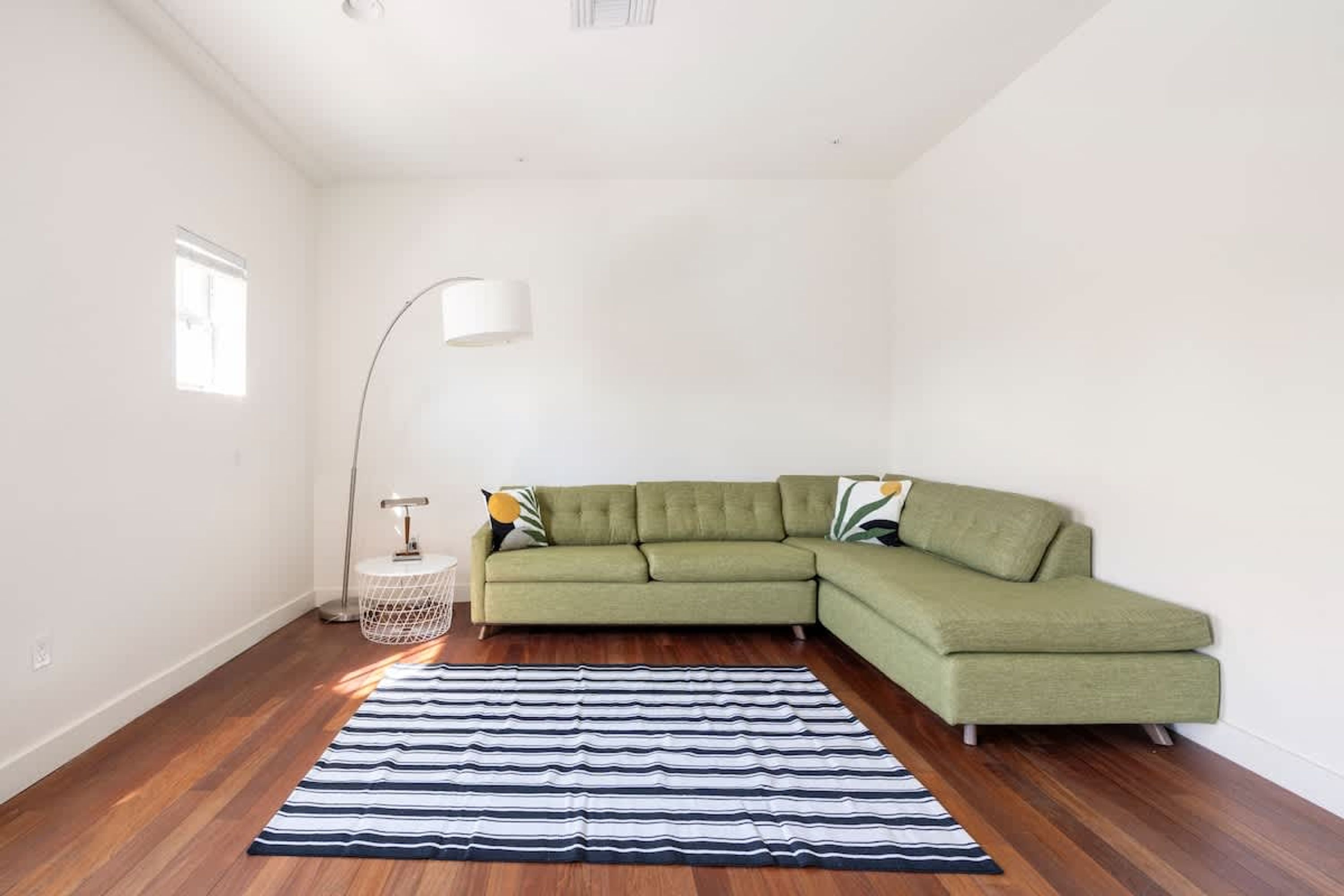 A modern living room with a green sectional sofa, a striped rug, and a floor lamp.