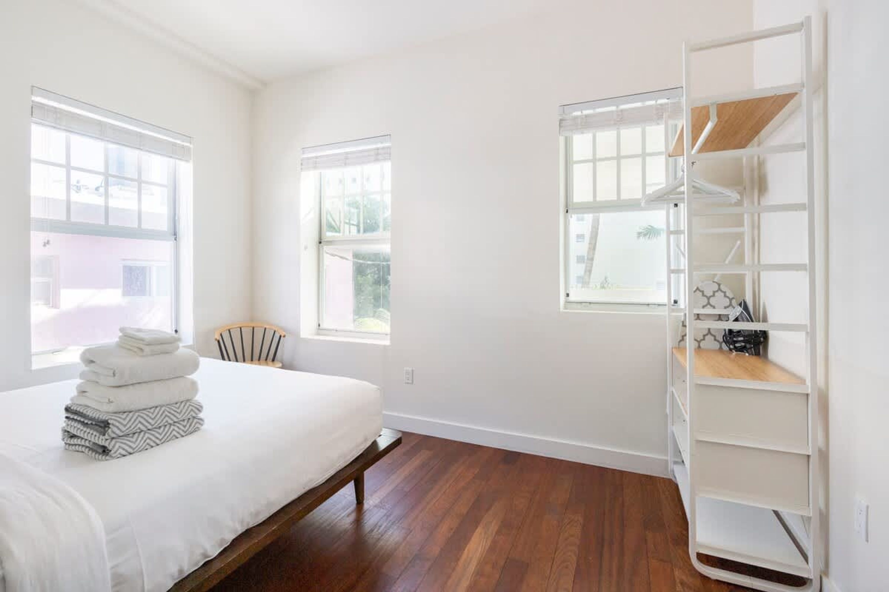 A bedroom with a bed, wooden flooring, white walls, and a built-in shelving unit.
