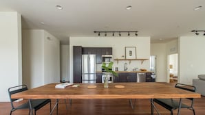 Une cuisine moderne avec des meubles de couleur sombre, des appareils en acier inoxydable et une table à manger en bois, accompagnée de chaises.
