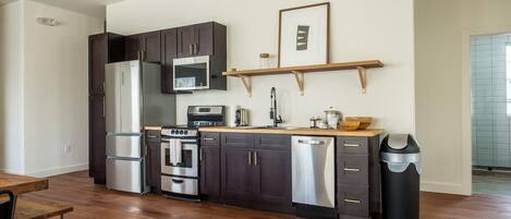 Una cocina moderna con armarios oscuros, electrodomésticos de acero inoxidable, una encimera de madera y un cubo de basura negro.